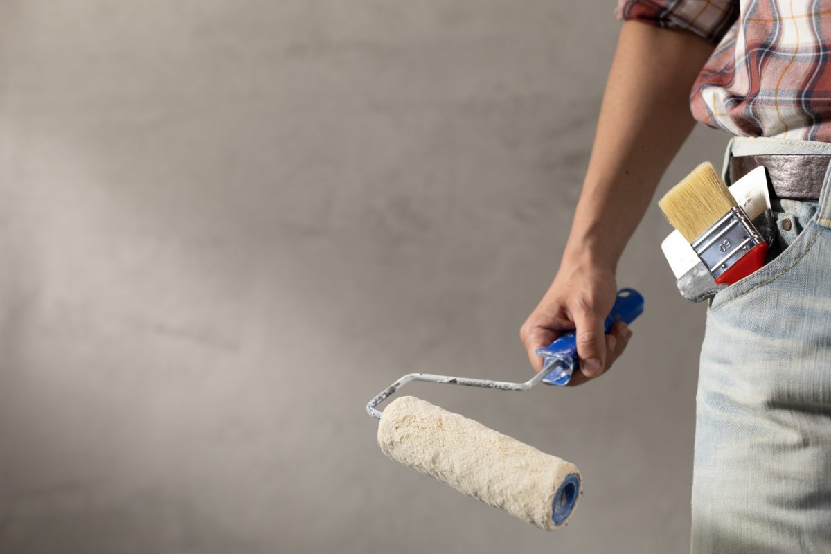 Construction worker man holding paint roller tool near concrete or plaster wall. Male hand and tools
